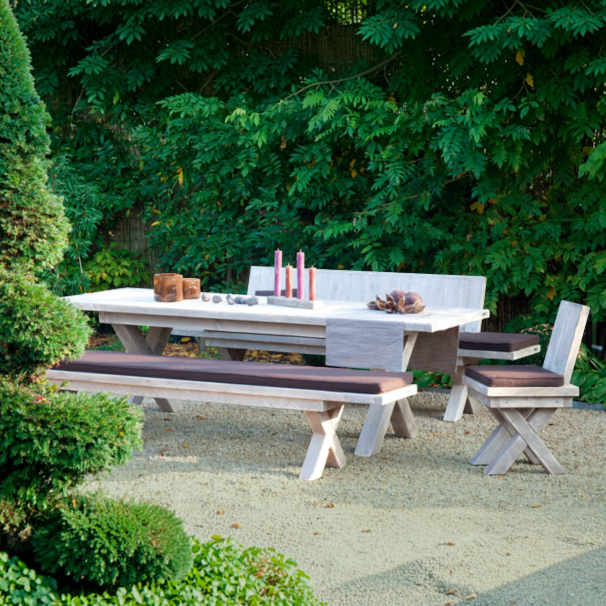 Helle Massivholz Sitzgruppe mit Tisch, Bänken mit Polstern und Stuhl auf Kies vor einer Hecke
