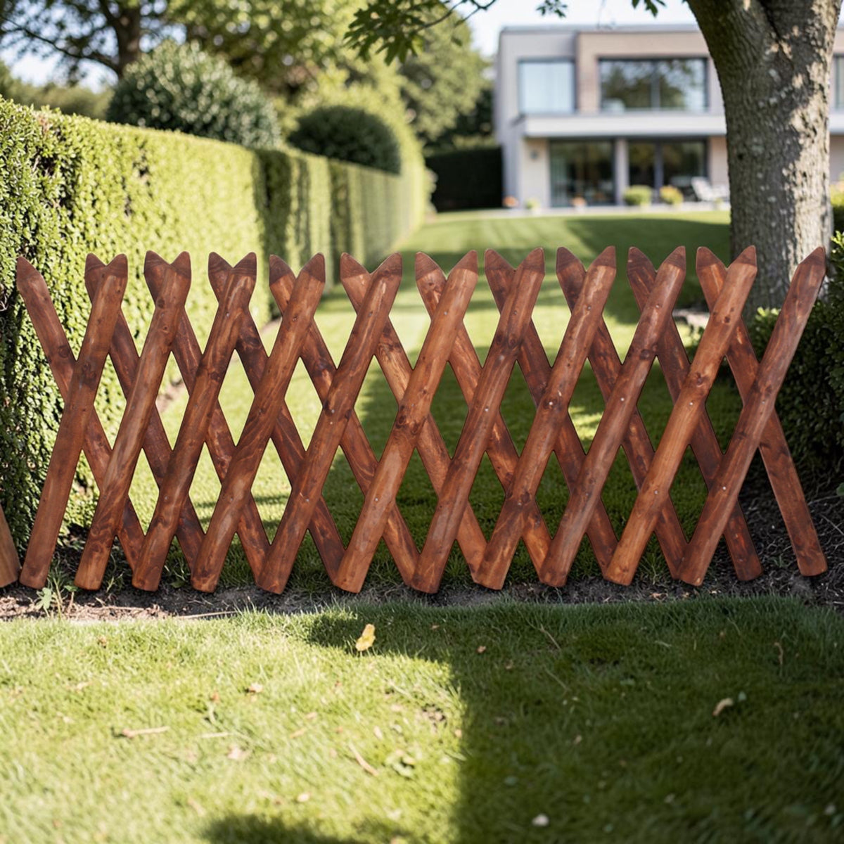 Jägerzaun aus braunem Holz vor einer Hecke im Garten eines Einfamilienhauses