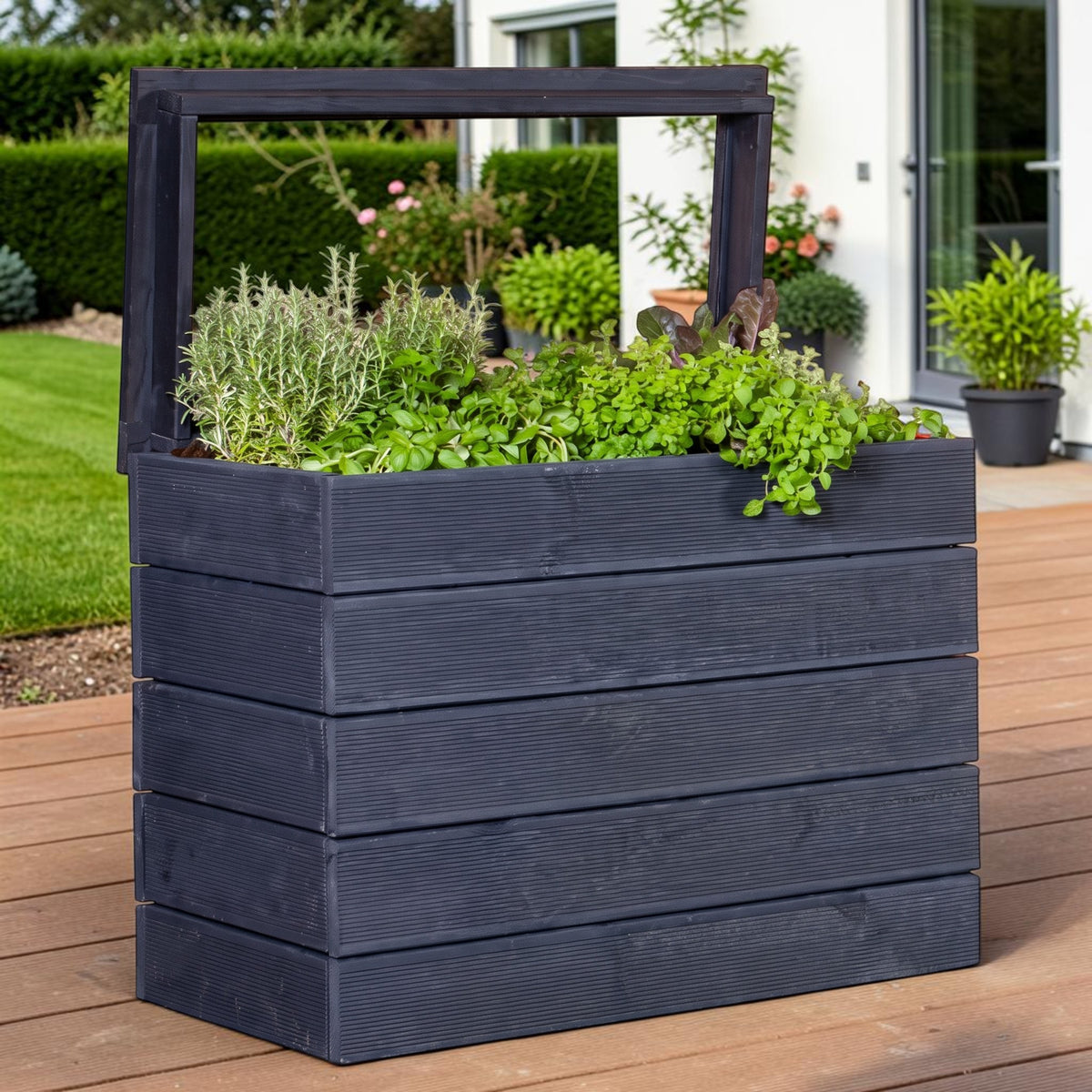 Lasiertes Hochbeet Ahre mit Kräutern auf einer Holzterrasse vor Rasen und Hecke