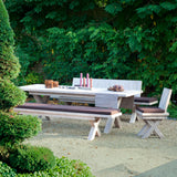 Helle Massivholz Sitzgruppe mit Tisch, Bänken mit Polstern und Stuhl auf Kies vor einer Hecke