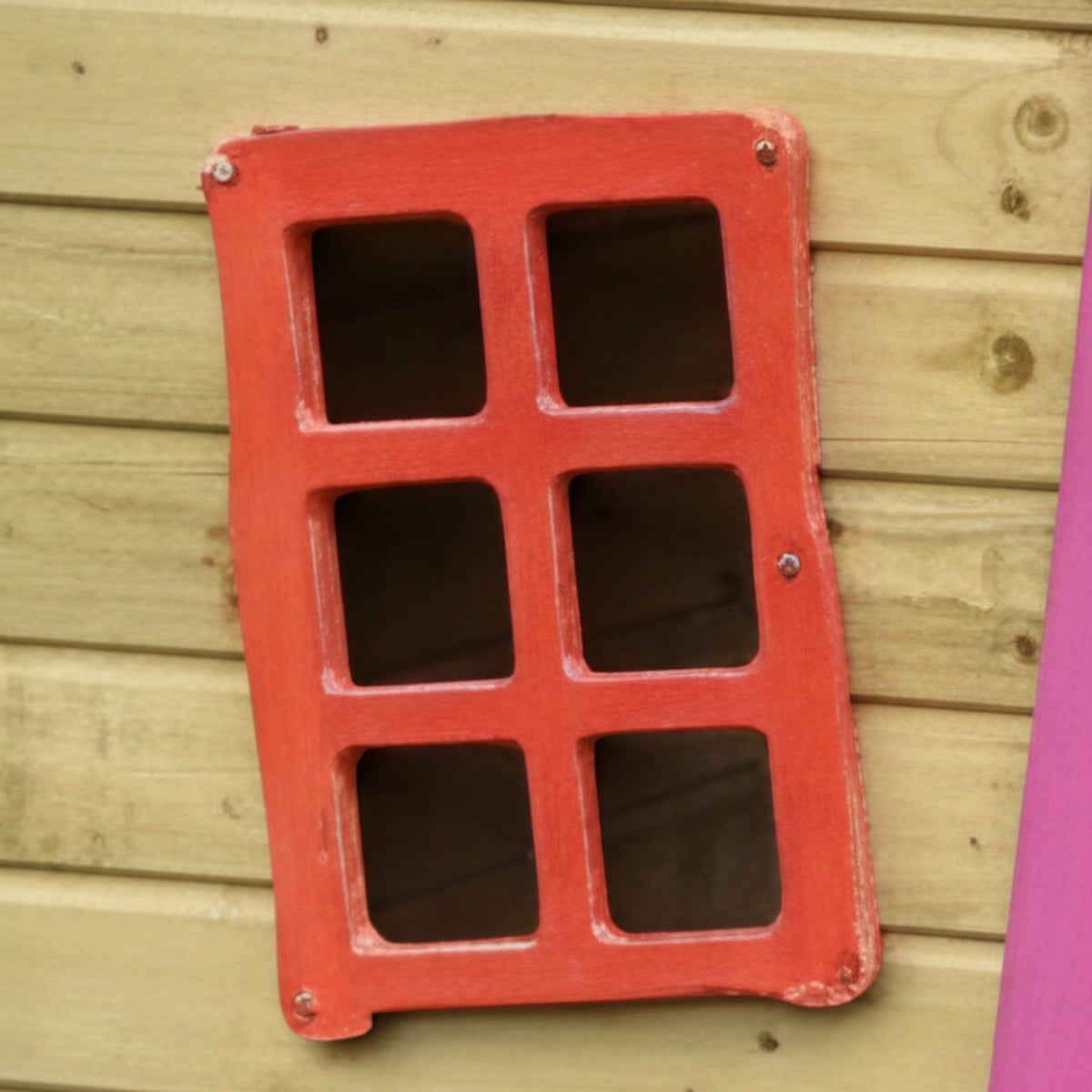 Rotes Sprossenfenster an der Holzwand des Kinderspielhauses im Detail