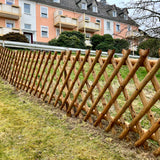 Jägerzaun aus braunem Holz als Grundstücksgrenze vor einem Mehrfamilienhaus