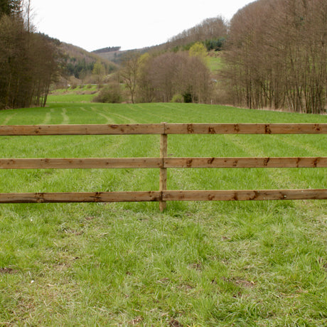 Plankenzaun aus Holz als Begrenzung einer Pferdekoppel vor Wald und Hügeln