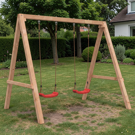 Holz Doppelschaukel mit roten Sitzen auf Rasen im Garten vor Hecke und Haus